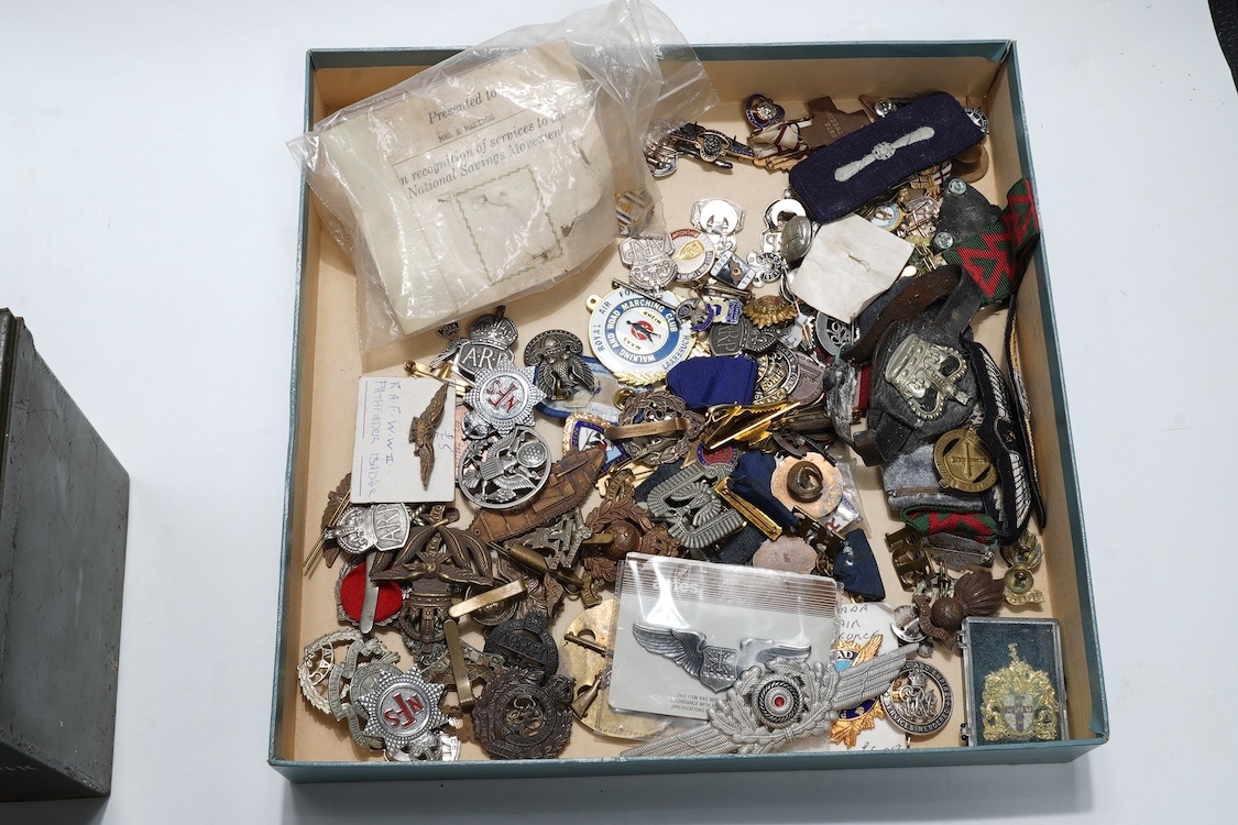 A collection of primarily 20th century military badges, lapel badges, shoulder titles, and other related ephemera, including seventeen military cap badges, cloth badges, ARP badges, etc., together with a military tin box